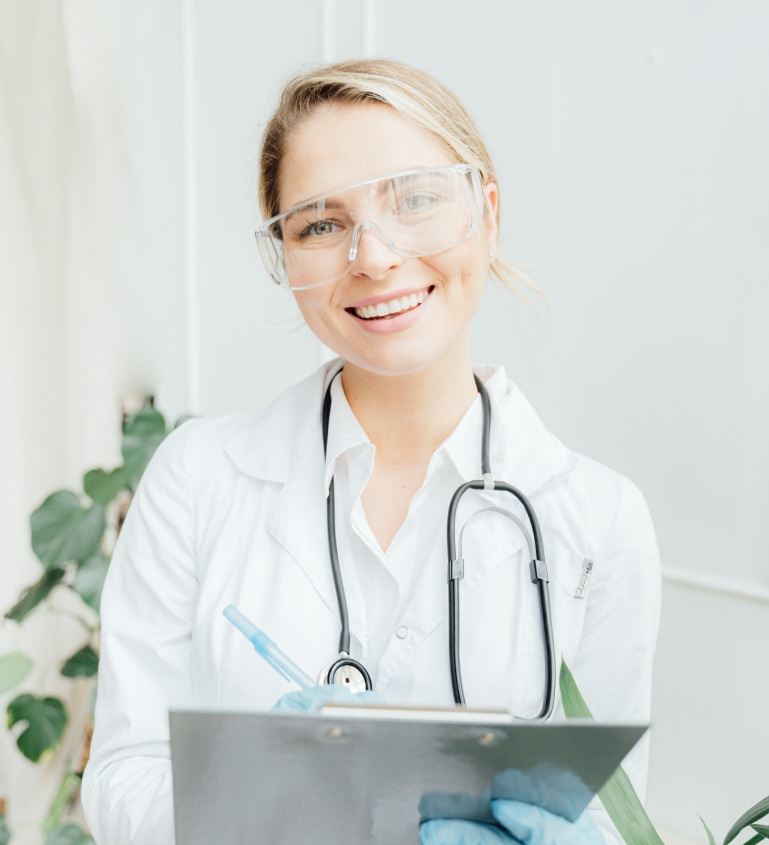 Smiling female doctor wearing protective glasses and gloves holding clipboard in medical office